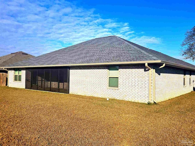 back of property with a sunroom, a shingled roof, brick siding, and a yard