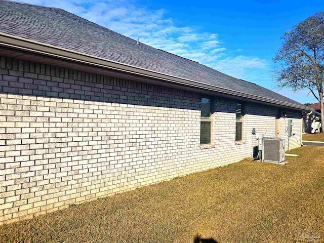 view of property exterior featuring a shingled roof, central AC unit, a lawn, and brick siding