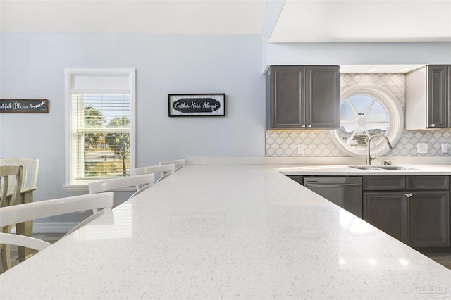 kitchen featuring sink, dishwasher, light stone counters, and decorative backsplash