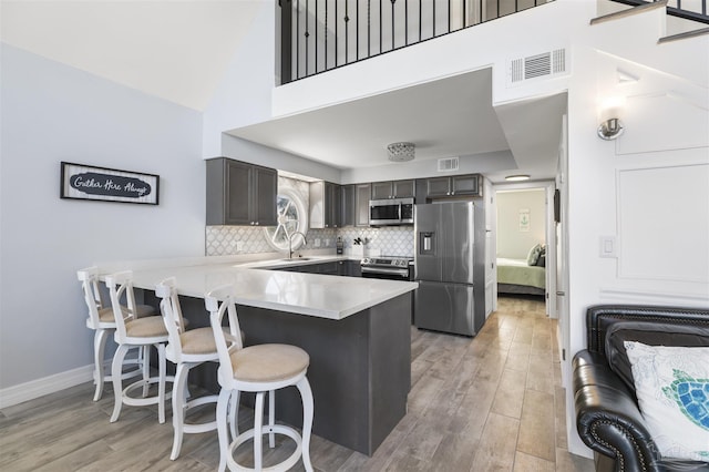 kitchen with kitchen peninsula, light hardwood / wood-style flooring, stainless steel appliances, high vaulted ceiling, and a breakfast bar area