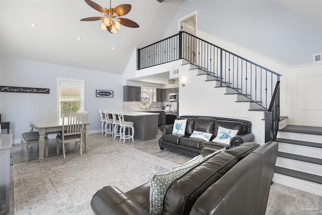 living room with high vaulted ceiling, ceiling fan, and light wood-type flooring