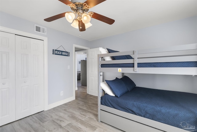 bedroom with stainless steel refrigerator, ceiling fan, light hardwood / wood-style floors, and a closet