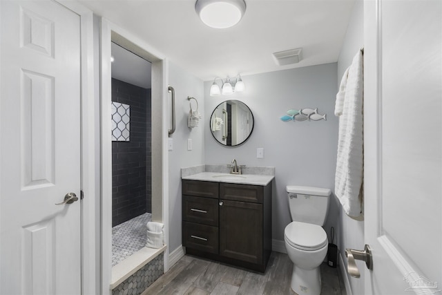 bathroom with toilet, hardwood / wood-style flooring, a tile shower, and vanity