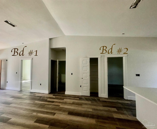 empty room with dark wood-style floors, visible vents, vaulted ceiling, and baseboards