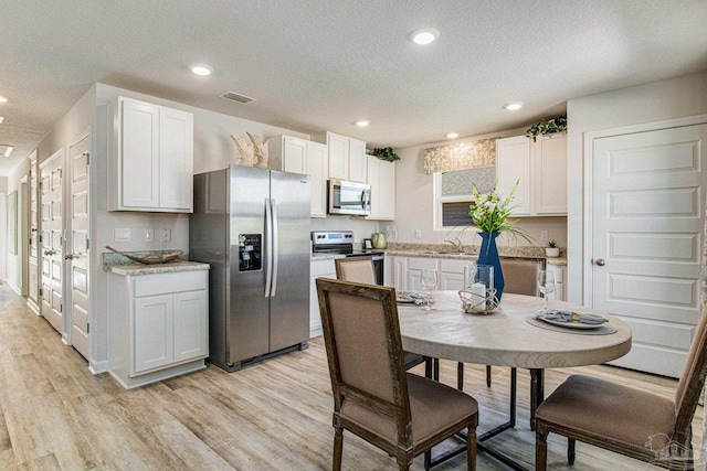 kitchen with appliances with stainless steel finishes, sink, white cabinets, a textured ceiling, and light hardwood / wood-style flooring