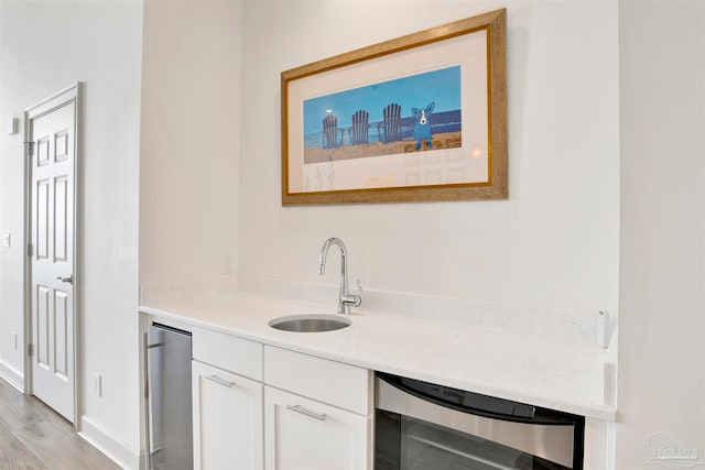 bar with light hardwood / wood-style floors, wine cooler, white cabinets, stainless steel refrigerator, and sink