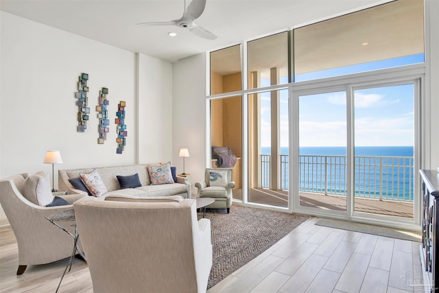 living room with ceiling fan, light hardwood / wood-style flooring, expansive windows, and a water view