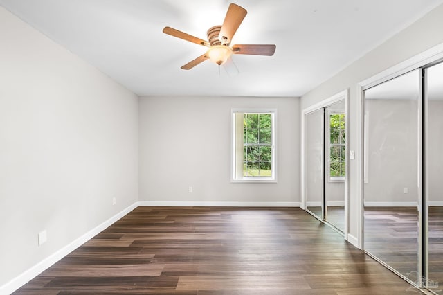 unfurnished bedroom with ceiling fan, baseboards, dark wood-type flooring, and two closets