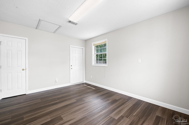 unfurnished room with baseboards, attic access, visible vents, and dark wood-style flooring