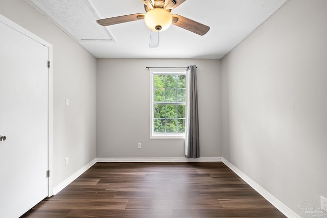 empty room with ceiling fan, dark wood finished floors, attic access, and baseboards