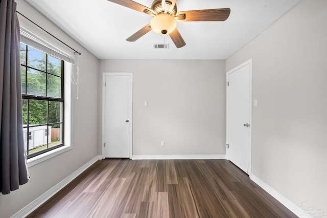 empty room with dark wood-style floors, a ceiling fan, visible vents, and baseboards