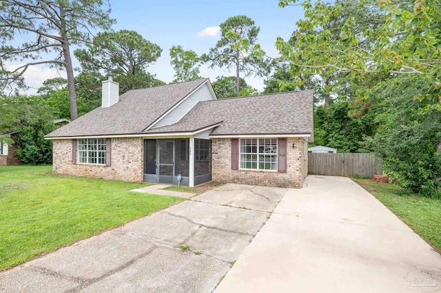 ranch-style home featuring brick siding, a chimney, a front yard, a sunroom, and fence