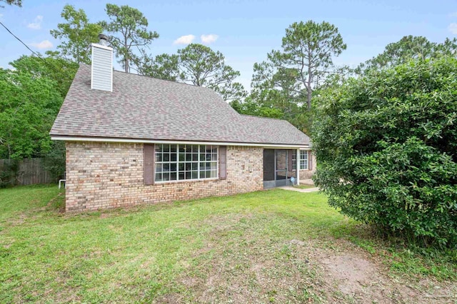 view of front facade with brick siding, roof with shingles, a chimney, and a front yard