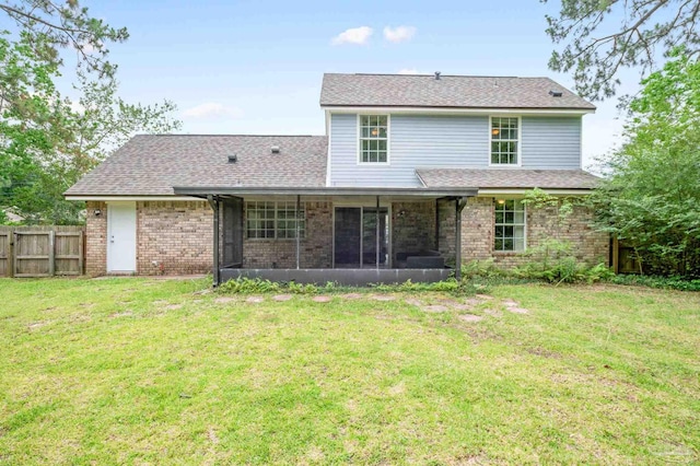 rear view of property featuring a sunroom, brick siding, a lawn, and fence