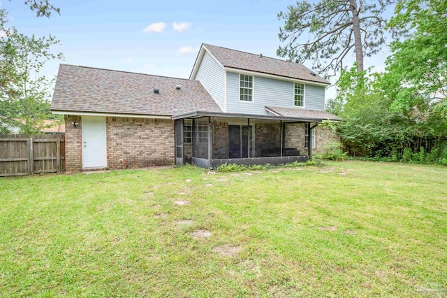 back of property with brick siding, a shingled roof, fence, a sunroom, and a lawn