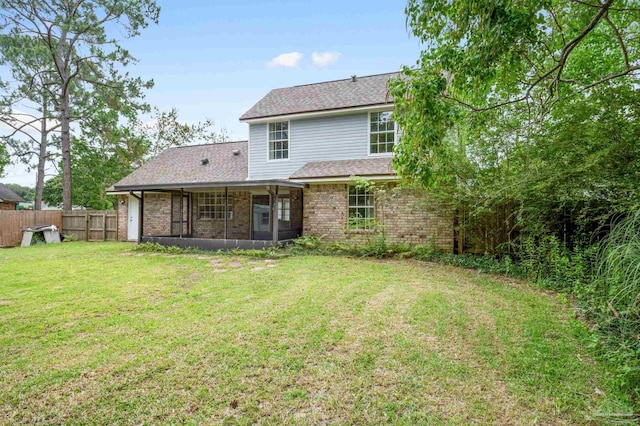 back of property featuring brick siding, a lawn, fence, and a sunroom