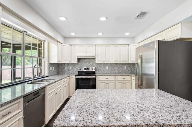 kitchen with light stone counters, stainless steel appliances, tasteful backsplash, visible vents, and a sink