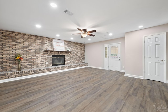 unfurnished living room featuring brick wall, ceiling fan, dark hardwood / wood-style floors, and a fireplace