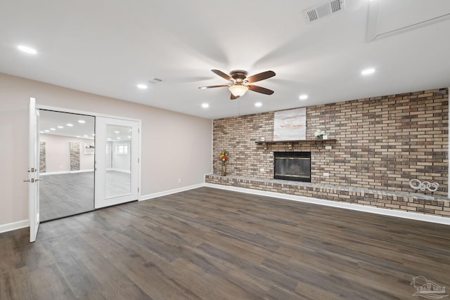 unfurnished living room featuring a fireplace, brick wall, ceiling fan, and dark hardwood / wood-style floors