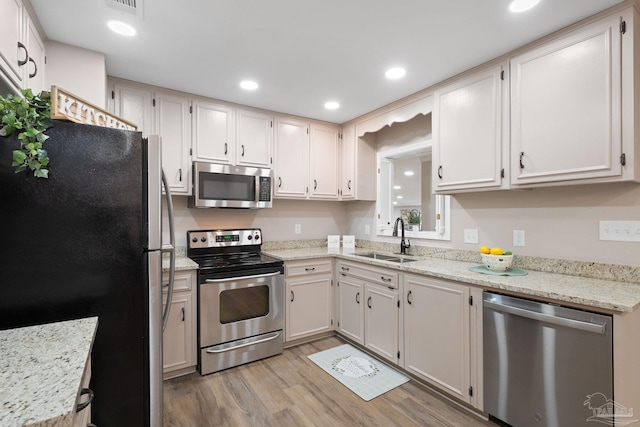 kitchen with sink, stainless steel appliances, light hardwood / wood-style flooring, and light stone counters