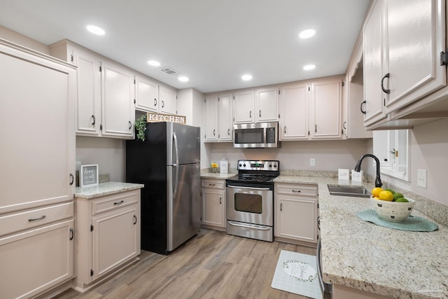 kitchen featuring light stone counters, light hardwood / wood-style floors, white cabinetry, appliances with stainless steel finishes, and sink