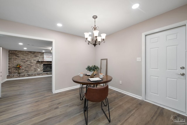 dining room featuring a notable chandelier, dark wood-type flooring, a brick fireplace, and brick wall