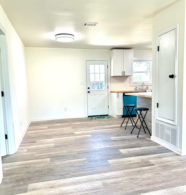 kitchen with a breakfast bar, white cabinets, visible vents, and light wood-type flooring