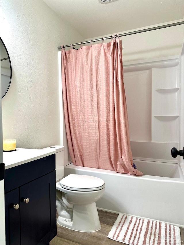 bathroom with toilet, wood finished floors, shower / tub combo, vanity, and a textured wall