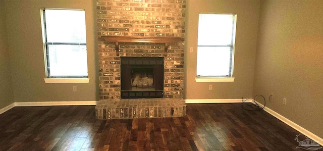 unfurnished living room featuring plenty of natural light, dark hardwood / wood-style floors, and a brick fireplace