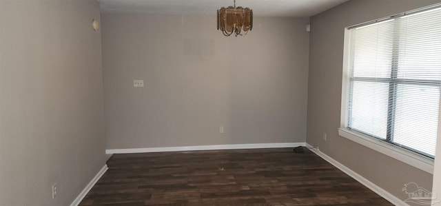 spare room with plenty of natural light, dark wood-type flooring, and an inviting chandelier