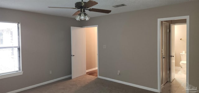 unfurnished bedroom featuring multiple windows, carpet floors, ensuite bathroom, and ceiling fan