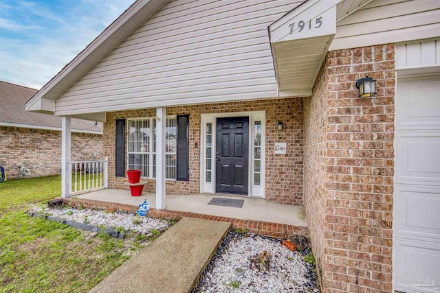 doorway to property with covered porch, brick siding, and a garage