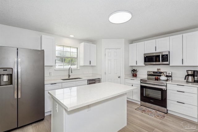 kitchen featuring appliances with stainless steel finishes, a sink, white cabinets, and light wood-style floors