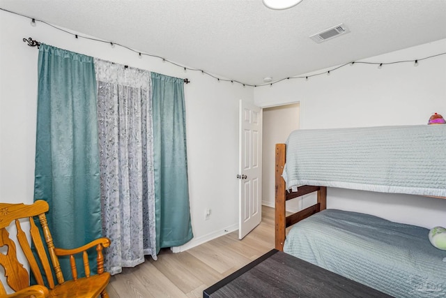 bedroom featuring a textured ceiling, wood finished floors, visible vents, and baseboards