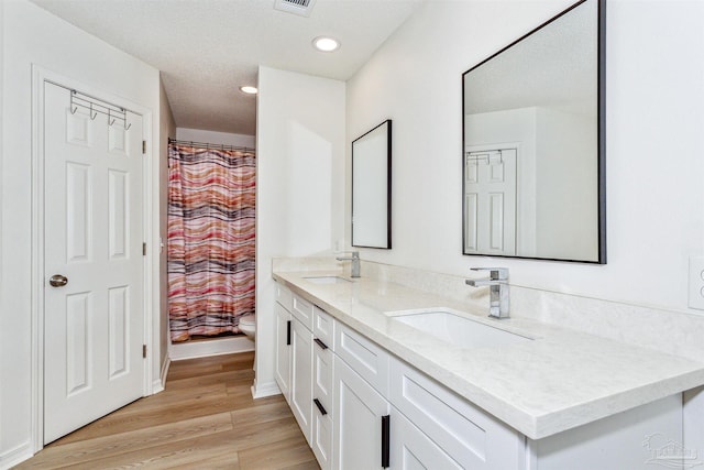 full bath featuring double vanity, a sink, toilet, and wood finished floors