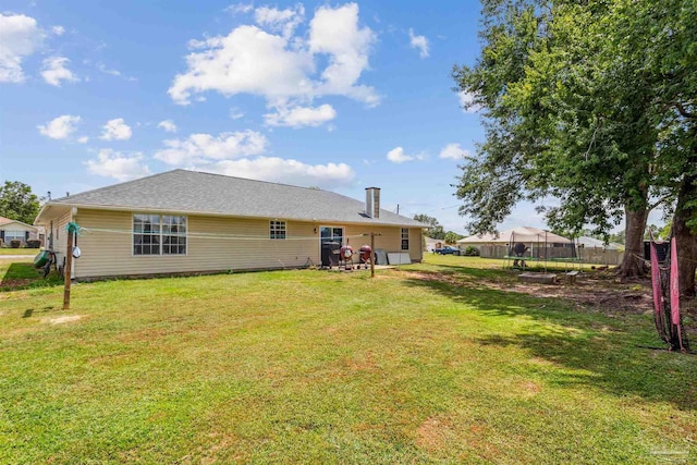 rear view of house with a trampoline, fence, and a yard