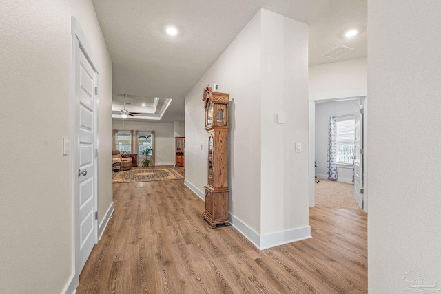 hallway with a tray ceiling, wood finished floors, visible vents, and baseboards