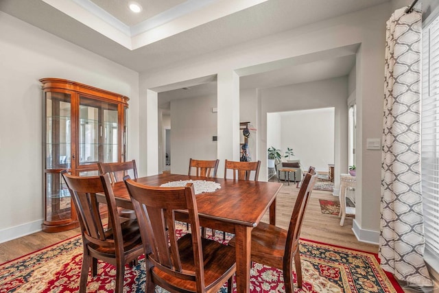 dining space featuring baseboards, recessed lighting, a raised ceiling, and light wood-style floors