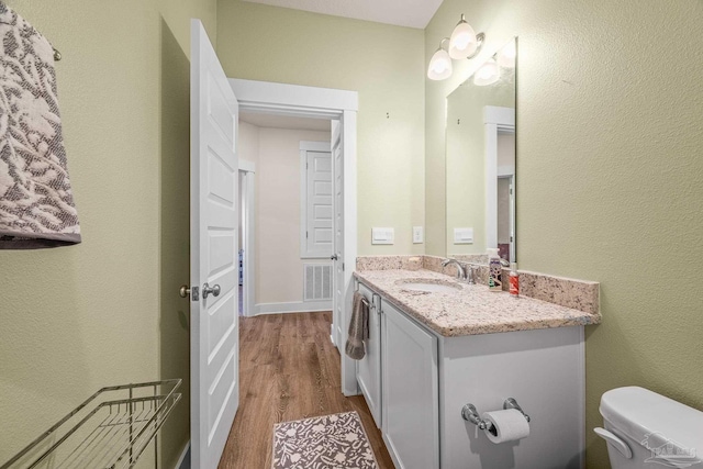 half bath featuring visible vents, vanity, toilet, and wood finished floors