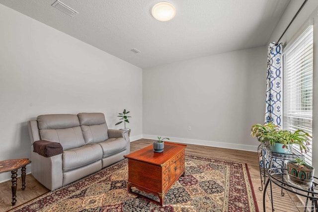 living area with a textured ceiling, wood finished floors, visible vents, and baseboards