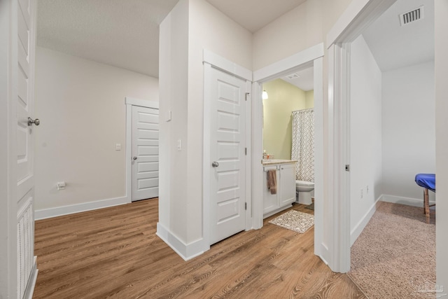 corridor featuring light wood-style floors, baseboards, and visible vents