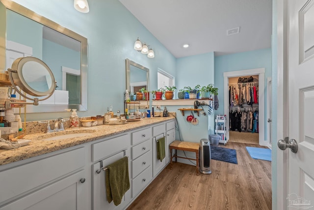 bathroom with double vanity, visible vents, wood finished floors, a spacious closet, and a sink