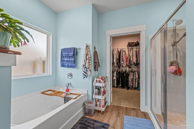 bathroom featuring a walk in closet, a garden tub, a shower stall, and wood finished floors