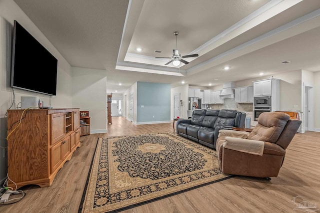 living room with baseboards, ceiling fan, a tray ceiling, light wood-type flooring, and recessed lighting