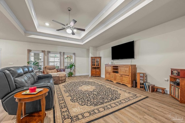 living room with ceiling fan, light wood-style flooring, baseboards, a tray ceiling, and crown molding