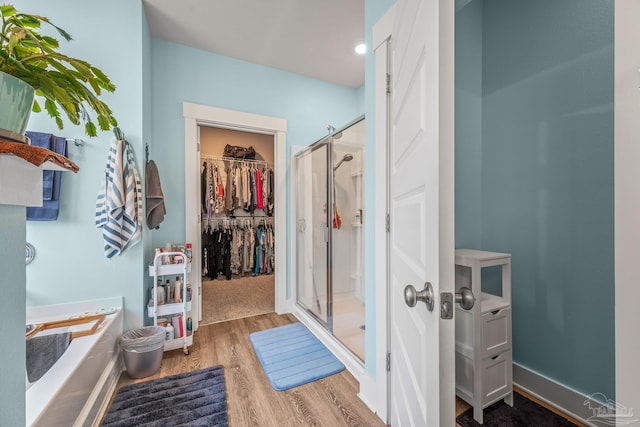 full bathroom featuring a bath, a stall shower, a spacious closet, and wood finished floors