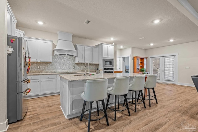 kitchen featuring stainless steel appliances, visible vents, light wood-style floors, decorative backsplash, and custom range hood