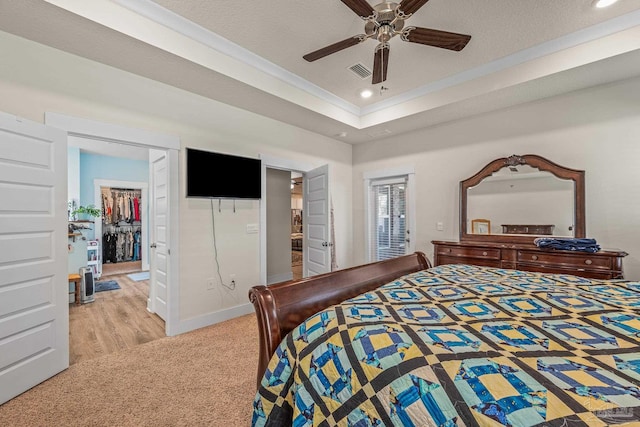 bedroom featuring a tray ceiling, a walk in closet, crown molding, recessed lighting, and visible vents