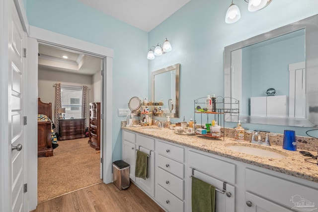 bathroom with double vanity, ensuite bath, a sink, and wood finished floors