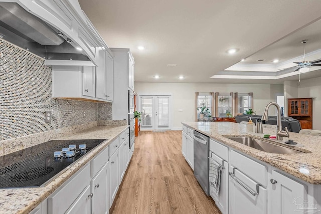 kitchen featuring a tray ceiling, stainless steel dishwasher, a sink, premium range hood, and black electric cooktop